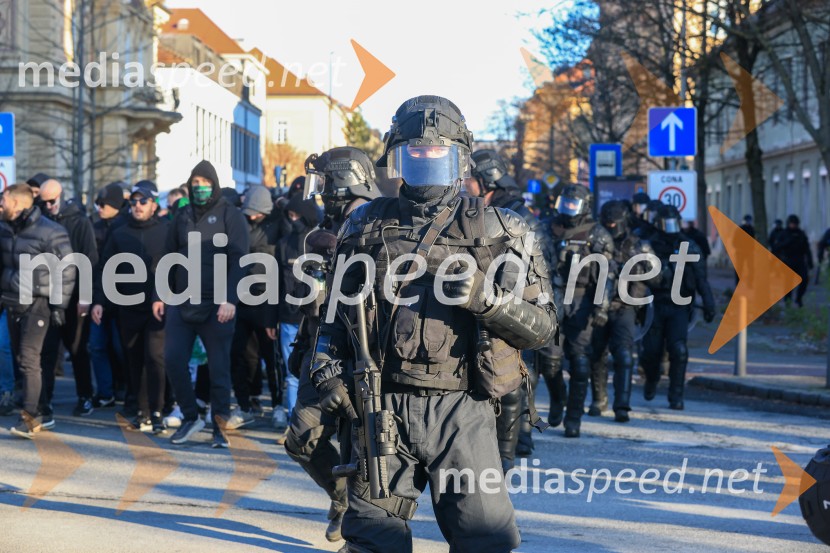 Policist v zaščitni opremi. Za njim prihaja navijaška skupina.Derbi v Ljudskem vrtu: Maribor in Olimpija brez zmagovalca pred 9.000 navijači